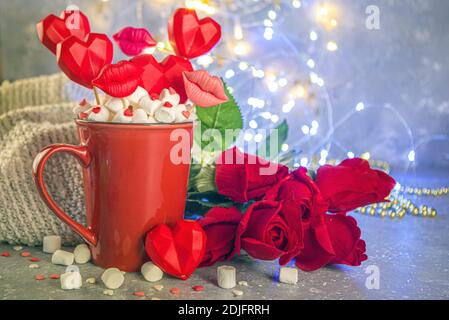 Valentine`s Day Süßwaren-Konzept, festliche Feiertagshintergrund mit heißer Schokolade rote Tasse und Set von roten Herzen Süßigkeiten auf Sticks in Tasse, mit roten Rosen und Stockfoto